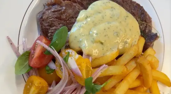 En saftig biff med krämig bearnaisesås, gyllene pommes frites och en fräsch tomatsallad. En klassisk steak frites-upplevelse.