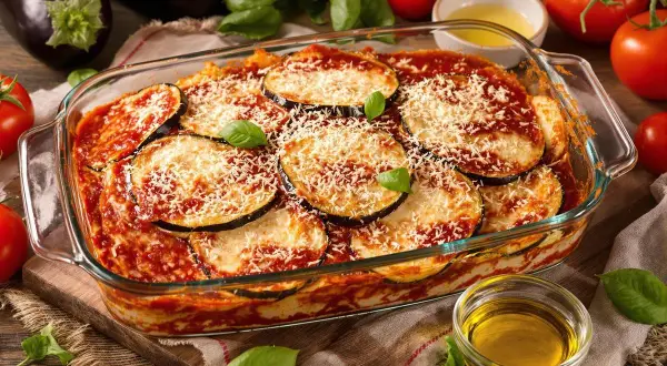 Un plat d'aubergine parmigiana tout juste sorti du four, garni de fromage râpé et de basilic frais.