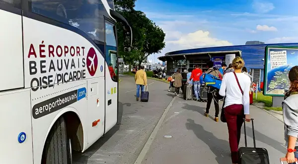 Autobus z napisem "AÉROPORT BEAUVAIS OISE/PICARDIE" czeka na pasażerów z walizkami przed terminalem.
