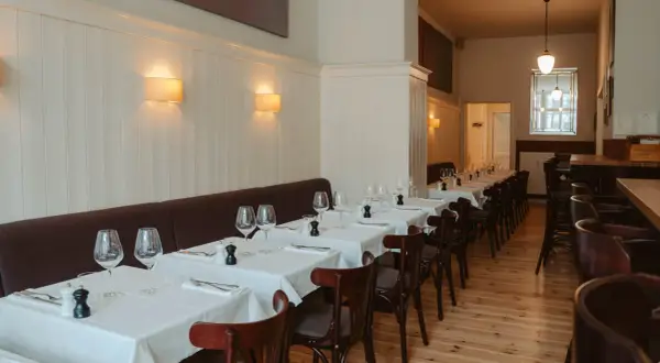 Elegantes Restaurant in Berlin, bereit für Gäste. Tische sind mit weißen Tischdecken, Gläsern und Besteck gedeckt. Gemütliche Atmosphäre dank Wandlampen.