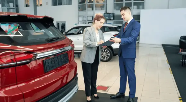 Kobieta podpisuje dokumenty przy nowej, czerwonej Toyocie. To jej pierwszy przegląd gwarancyjny.