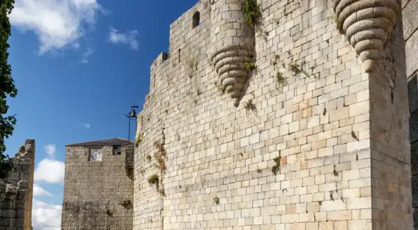 Muros de piedra de un castillo medieval en Castro Caldelas. Un torreón con matacanes y una torre con reloj son parte de lo que ver.