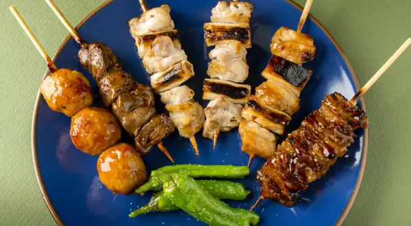 Różnorodne yakitori na niebieskim talerzu: kurczak, wątróbka, kulki mięsne i papryczki shishito.