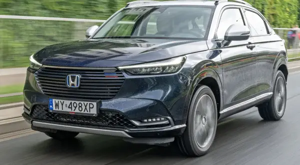 Ciemnogranatowy Honda HR-V na mokrej drodze. Nowoczesne reflektory i grill podkreślają jego dynamiczny charakter. Silniki tej generacji zapewniają oszczędność i płynność jazdy.