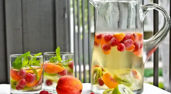 Orzeźwiająca sangria drink z malinami, brzoskwiniami i kiwi w dzbanku i szklankach, ozdobiona miętą.