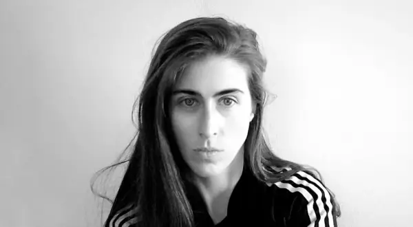 Ritratto in bianco e nero di Mara Oscar Cassiani, con lunghi capelli castani e indosso una felpa con le iconiche tre strisce.