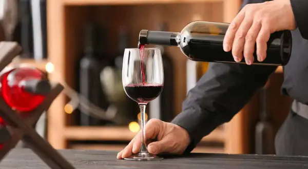 Versando vino rosso in un bicchiere, si notano i difetti del vino: torbidità e sedimenti.