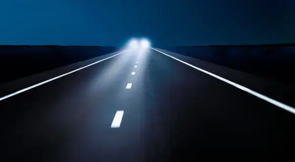 Nocna droga z jasnymi światłami mijania, które oświetlają białe linie.