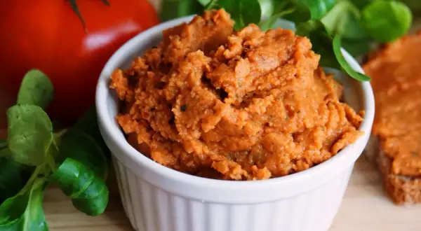 Pyszna, domowa pasta z soczewicy w białej miseczce, obok pomidora i świeżej zieleniny. Idealna na kanapki.