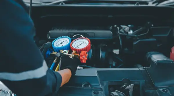 Tecnico con guanti controlla i manometri per ricaricare aria condizionata auto.