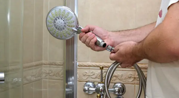 Mann wechselt die duschbrause. Er hält die alte Brause in der Hand und den Schlauch daneben.