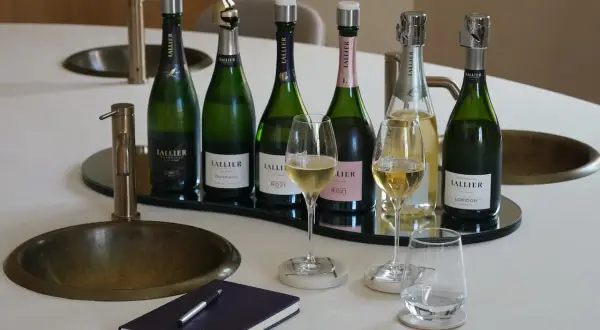 Sechs Flaschen LALLIER Champagner, vielleicht der beste Champagner der Welt, stehen bereit. Zwei Gläser sind gefüllt, bereit für eine Verkostung.