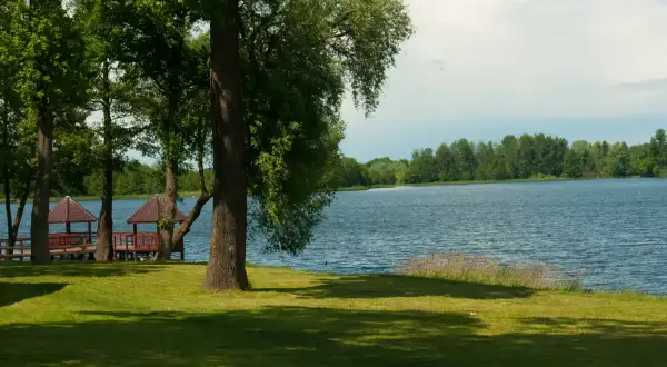 Malownicze jezioro Zelwa otoczone zielenią, z drewnianymi altankami przy brzegu.
