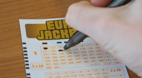 Dłoń z długopisem zaznacza liczby na kuponie Eurojackpot.