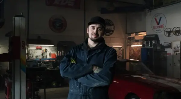 Mechanik w warsztacie z czerwonym autem. Co zrobić, gdy mechanik przetrzymuje auto? Zapytaj o fakturę i termin odbioru.