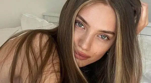 Kobieta z brązowymi włosami i pasemkami blond na przodzie, leżąca na łóżku.