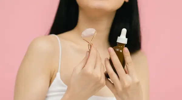 Kobieta z aparatem na zębach trzyma masażer do twarzy i serum. Czy wiesz, że retinol to witamina A, kluczowa dla zdrowej skóry?