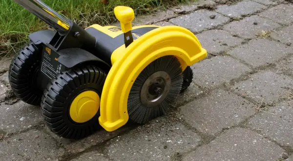 Żółta elektryczna zamiatarka do kostki z czarnymi kołami i szczotką, gotowa do pracy na podjeździe.