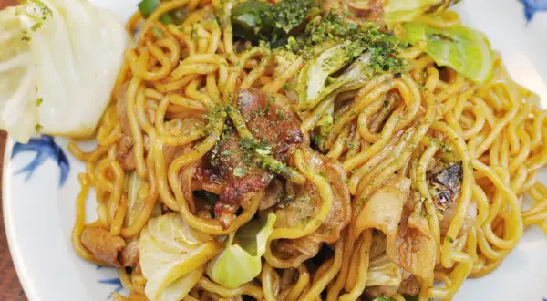 Yaki soba mit Schweinefleisch und Kohl, garniert mit grünen Kräutern. Ein köstliches Gericht, das zum Genießen einlädt.