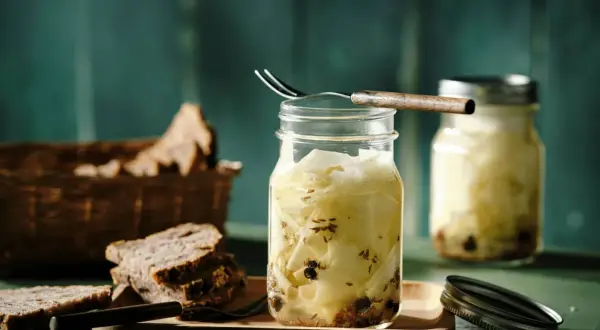 Kohlrabi fermentieren: Gläser mit eingelegtem Kohlrabi, Gewürzen und Brot im Hintergrund.