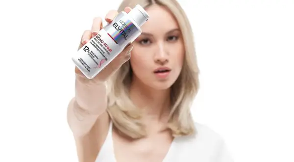 Frau zeigt L'Oréal Elvital Bond Repair Pre-Shampoo gegen extrem trockene Haare. Vorher-Nachher-Effekt für geschädigtes Haar.