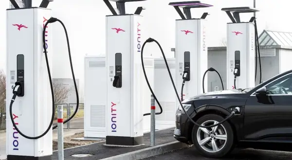 Une voiture électrique noire est branchée à une borne de recharge Ionity. Plusieurs bornes sont alignées, prêtes à alimenter les véhicules.