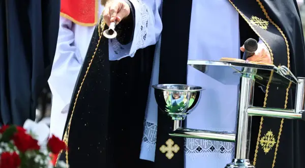 Osoba w szatach liturgicznych sypie ziarna. Czy to apostata, kto to? Ceremonia z mikrofonem i kielichem.
