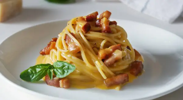 Spaghetti carbonara – przepis oryginalny ze śmietaną. Pyszne danie z makaronem, boczkiem i kremowym sosem jajeczno-serowym, udekorowane bazylią.