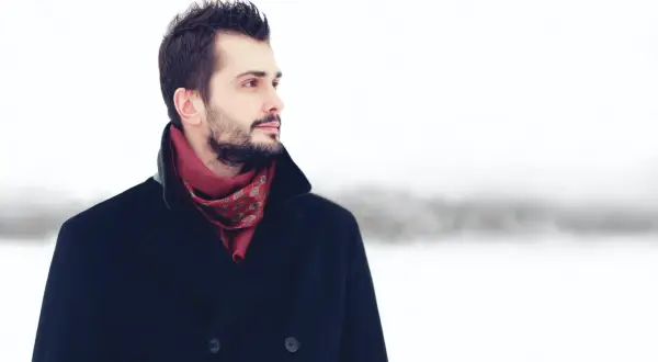 Mężczyzna w granatowym płaszczu i czerwonym, wzorzystym szaliku, na tle zimowego krajobrazu. Idealny przykład, jaki szalik do granatowego płaszcza.