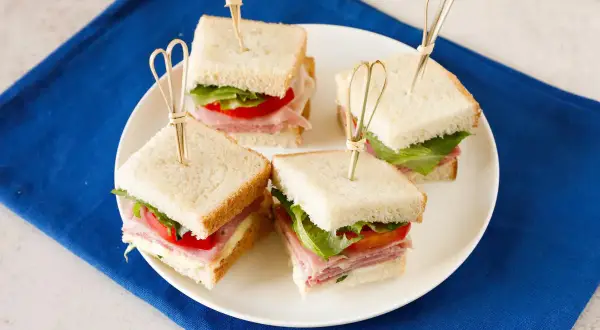 Quattro tramezzini quadrati con prosciutto, lattuga e pomodoro, perfetti per idee gusti tramezzini veloci e sfiziosi.