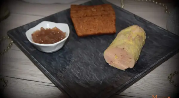 Un morceau de foie gras, une compotée de fruits et une tranche de pain d'épices sur une assiette. La cuisson du foie gras à l'eau bouillante est une méthode délicate.