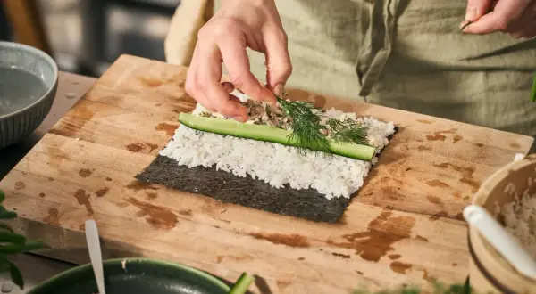 Händer lägger dill på egen sushi med ris, gurka och nori.