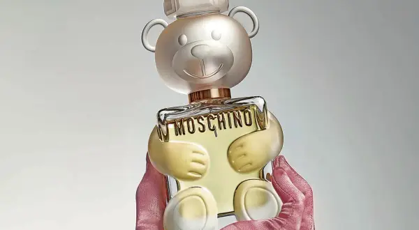 Różowe rękawiczki trzymają uroczy flakon perfum Moschino Toy 2 w kształcie misia.