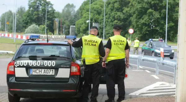 Funkcjonariusze Służby Celno-Skarbowej w kamizelkach odblaskowych przy radiowozie. Ich praca to nie tylko służba, ale też zarobki.
