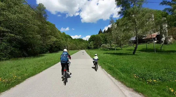 Dwie osoby na rowerach przemierzają malownicze **ojcowskie park narodowy trasy rowerowe**. Słoneczny dzień, zieleń i chmury na niebie.