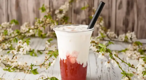 Jak zrobić bubble tea? Pyszny napój z truskawkowym syropem i mleczną pianką, ozdobiony kwitnącymi gałązkami.