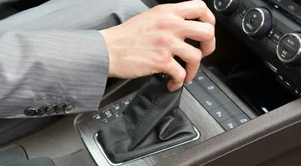 Pierwsza jazda automatem. Dłoń w garniturze zmienia bieg w samochodzie.