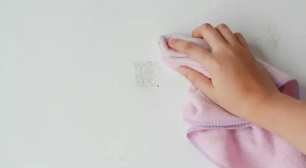 Handen torkar bort klisterrester från en målad vägg med en rosa trasa.