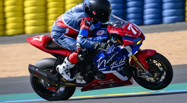 Motocyklista w niebiesko-czerwonym kombinezonie na torze wyścigowym, z tyłu żółte i niebieskie bandy.