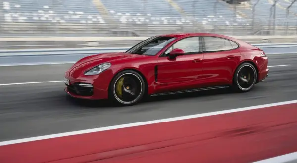 Czerwone Porsche Panamera GTS pędzi po torze wyścigowym, za nim widać trybuny.