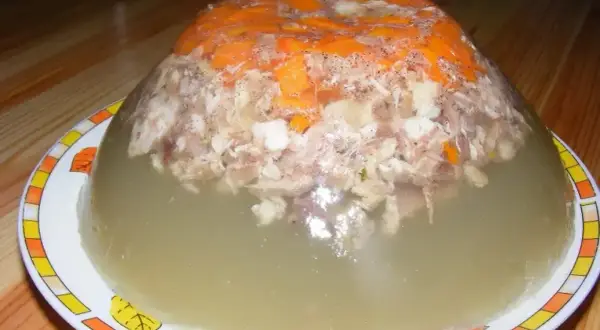 Pyszna galareta z golonki, z kawałkami mięsa i marchewki, w przezroczystej, galaretowatej masie.
