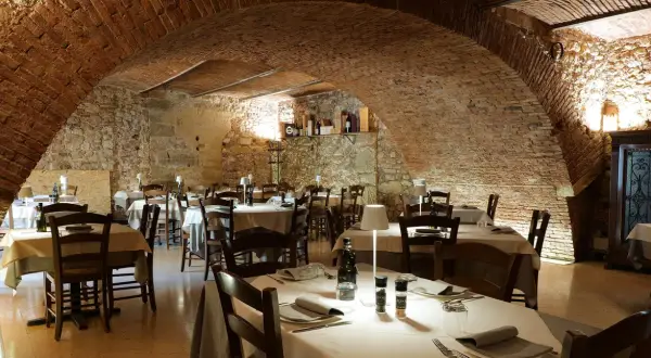 Interno di un ristorante con tavoli apparecchiati, soffitto a volta in mattoni e pareti in pietra. Un'atmosfera accogliente, ideale per scoprire i migliori ristoranti di Verona.