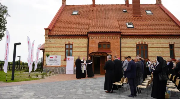 Uroczyste otwarcie centrum pomocowego Caritas im. Jana Pawła II. Grupa duchownych i wiernych zgromadzona przed budynkiem.