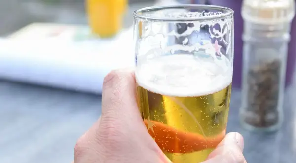 Dłoń trzymająca szklankę złotego piwa z pianką. Idealne piwo dla kobiet na letni wieczór.