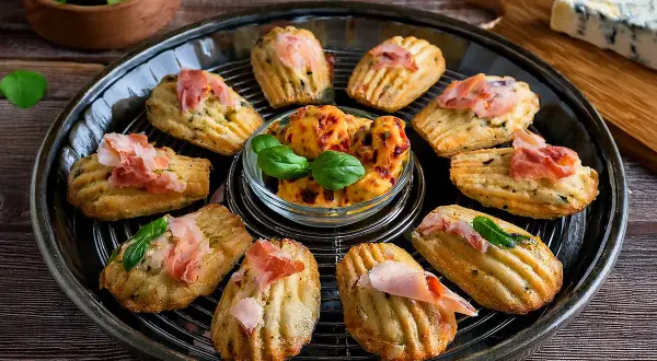 Délicieuses madeleines salées pour apéritif, garnies de jambon cru et de basilic. Parfaites pour une recette facile et gourmande.