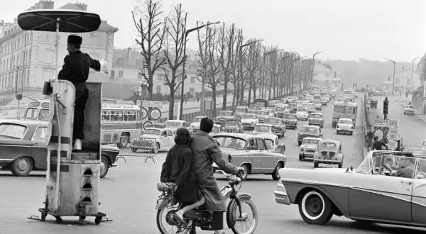 Un agent régule la circulation sur ce qui semble être la première autoroute de France, avec une file de voitures et un couple sur une mobylette.