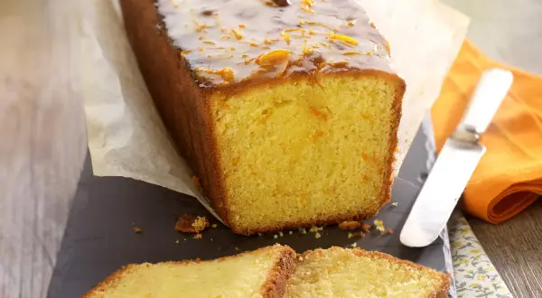 Wilgotne ciasto pomarańczowe z błyszczącą glazurą i kandyzowanymi skórkami pomarańczy, pokrojone na kromki.