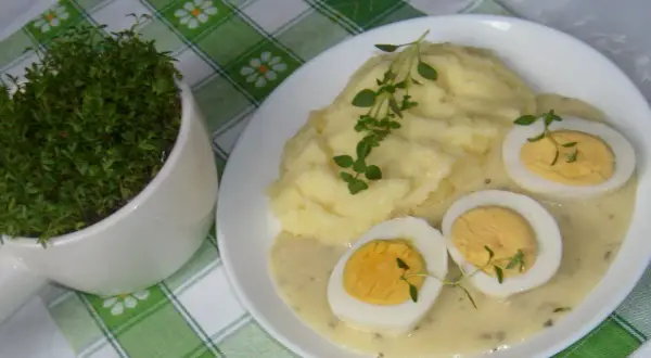 Pyszne ziemniaki puree z jajkami w sosie chrzanowym na ciepło, udekorowane gałązkami ziół. Obok doniczka ze świeżą rzeżuchą.