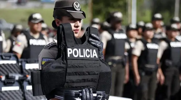 Agente de policía sostiene chaleco antibalas de material kevlar. Detrás, otros agentes uniformados.