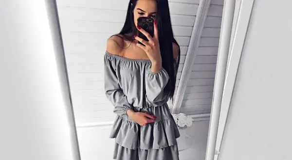 Dziewczyna w szarej sukience hiszpance z falbankami, która wygląda jak sukienki hiszpanki długie, robi sobie selfie w lustrze.